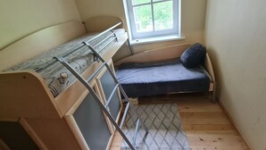 Une petite pièce avec un lit superposé, un lit simple, une fenêtre et un tapis à motifs.