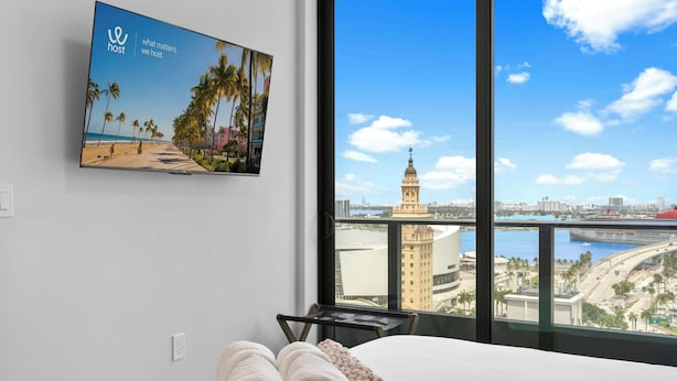 Ein Hotelzimmer mit großem Fenster, einem Strandbild und Blick auf eine Stadtlandschaft.