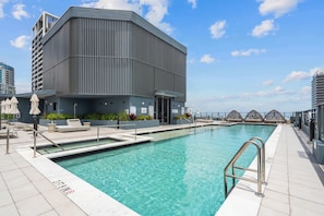 A modern building with a pool, outdoor seating, and a clear sky. - Modern 1BR | Gym / Pool | 10 Min to FIFA Fan Fest (Miami)