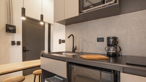 Une cuisine moderne équipée d’un lave-vaisselle en acier inoxydable, d’une machine à café et de tabourets en bois.