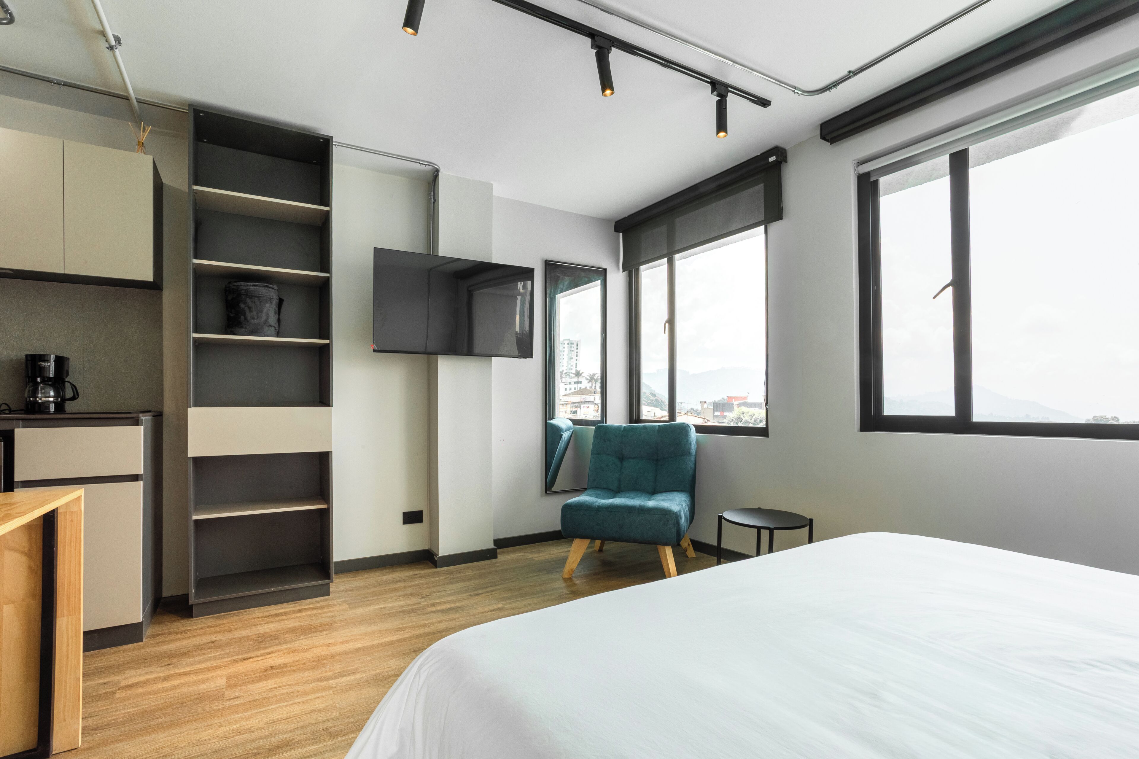 Et moderne hotelværelse med en seng, en stol, et TV ophængt på væggen og udsigt over byen gennem store vinduer.