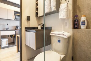 A modern bathroom with a toilet, a glass shower enclosure, a sink, and a countertop with toiletries. - Break Estudios Manizales (Manizales)