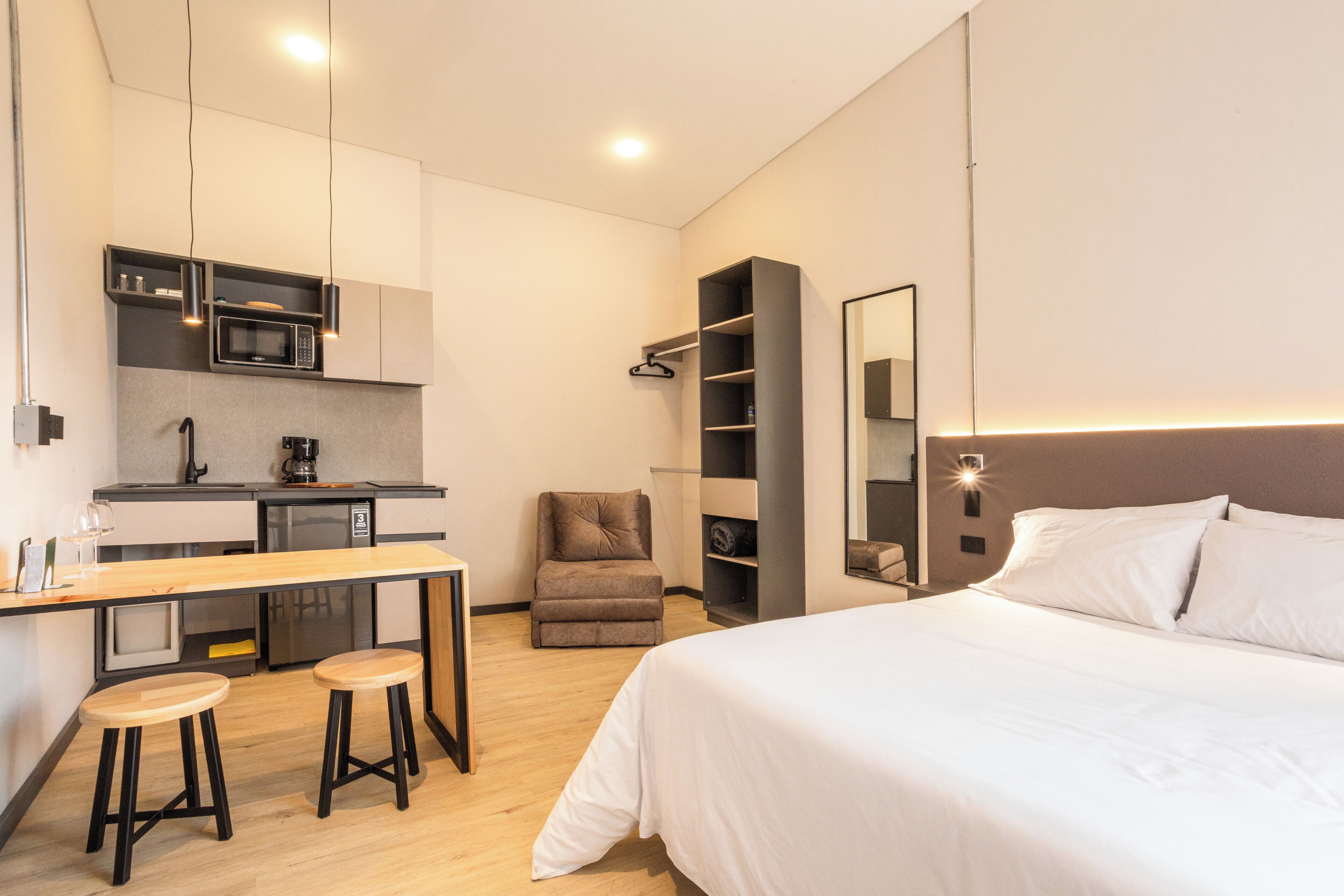 Une chambre d’hôtel moderne équipée d’un lit, d’un bureau avec des tabourets, d’un micro-ondes, d’une chaise et d’une bibliothèque.