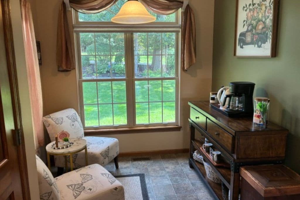 A cozy room with a window, a chair, a small table, and a dresser with a coffee maker.