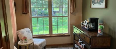 A cozy room with a window, a chair, a small table, and a dresser with a coffee maker.