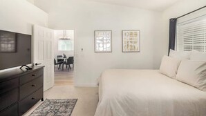 Un dormitorio con cama, televisor, cómoda y cuadros en la pared.