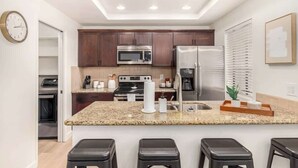 Una cocina moderna con encimeras de granito, electrodomésticos de acero inoxidable y una isla central con taburetes de bar.