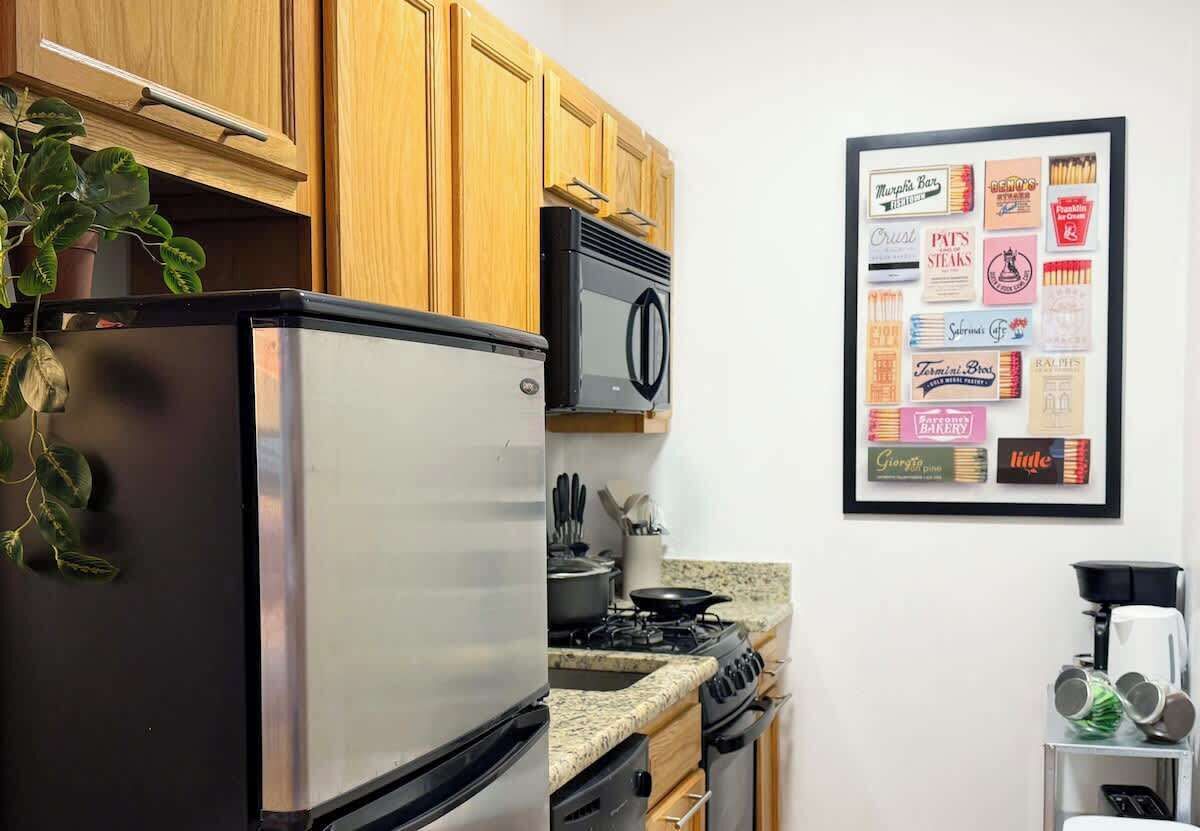 A kitchen with wooden cabinets, a stainless steel refrigerator, a stove, and a framed menu on the wall.