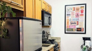 Een keuken met houten kastjes, een roestvrijstalen koelkast, een fornuis en een menukaart in een lijst aan de muur.