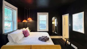 Een hotelkamer met een bed, twee ramen, een deur en een spiegel aan de muur.