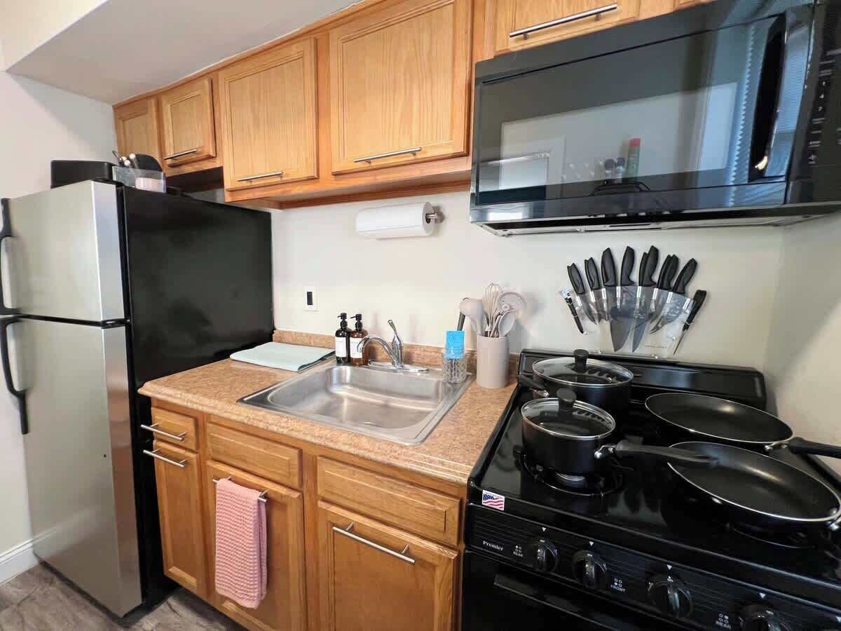 A kitchen with wooden cabinets, a stainless steel refrigerator, a microwave, a sink, and a stove.