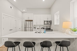 A modern kitchen with white cabinets, stainless steel appliances, a large island with bar stools, and a window with blinds. - Fifa Stay 1BR King Bed Sleeps 4 Near Everything (Conshohocken)