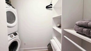 A laundry room with stacked washers and dryers, shelves with towels, and a basket. - Pride Weekend | Balcony | Renovated Church Loft (Philadelphia)
