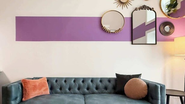 A modern living room with a dark green sofa, two cushions, a remote control on a coffee table, and decorative wall mirrors. - Pride Weekend | Balcony | Renovated Church Loft (Philadelphia)