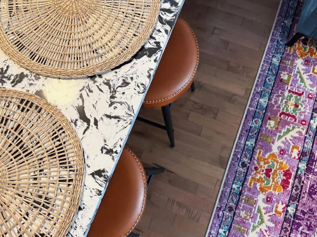A dining area with a table and chairs, a woven placemat, and a patterned rug on the floor.