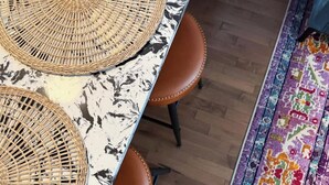 A dining area with a table and chairs, a woven placemat, and a patterned rug on the floor. - Pride Weekend | Balcony | Renovated Church Loft (Philadelphia)