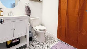 A bathroom with a toilet, a sink, a mirror, and a shower curtain. - Pride Weekend | Balcony | Renovated Church Loft (Philadelphia)