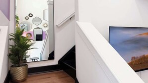 A hallway with a large mirror, a potted plant, and a painting on the wall. - Pride Weekend | Balcony | Renovated Church Loft (Philadelphia)