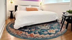 A bedroom with a bed, a patterned rug, a nightstand, a lamp, and a wall with a purple accent. - Pride Weekend | Balcony | Renovated Church Loft (Philadelphia)