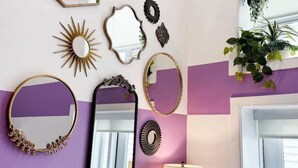 A wall with various mirrors and wall art, a window with plants, and a door. - Pride Weekend | Balcony | Renovated Church Loft (Philadelphia)
