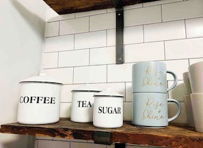 Des boîtes de rangement pour la cuisine, étiquetées « CAFÉ », « THÉ » et « SUCRE », sont rangées sur une étagère.