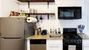 A kitchen with a stainless steel refrigerator, a black stove, a microwave, and white cabinets. - FIFA Walkable King Bed 3 Beds (Philadelphia)