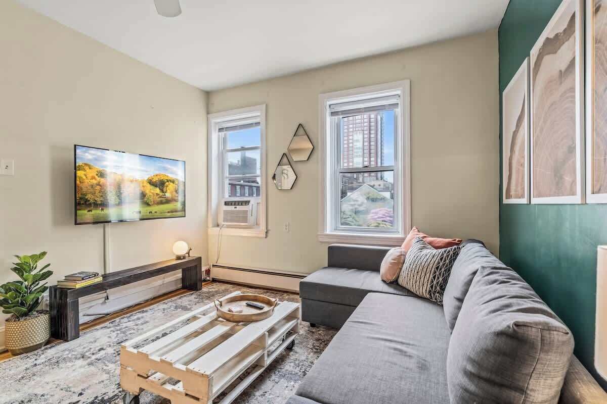 A living room with a flat-screen TV, a sofa, a coffee table, and a window with a city view.
