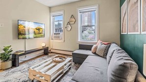 A living room with a flat-screen TV, a sofa, a coffee table, and a window with a city view. - Historic | Parking | Walk Score 98 | Cozy (Philadelphia)