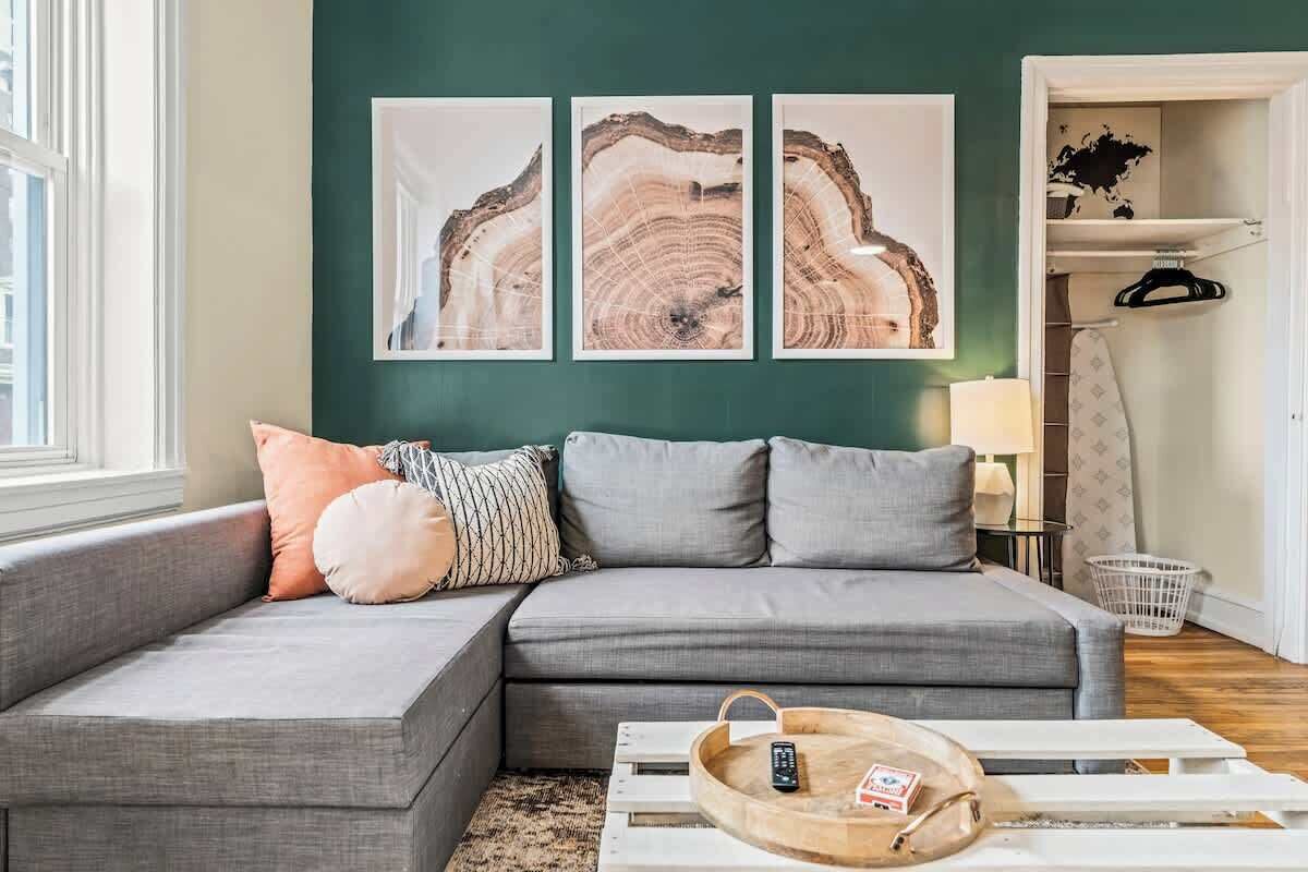 A modern living room with a grey sectional sofa, a wooden coffee table with a remote control, and three abstract art pieces on the wall.