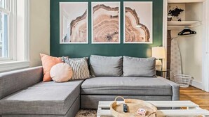 A modern living room with a grey sectional sofa, a wooden coffee table with a remote control, and three abstract art pieces on the wall. - Historic | Parking | Walk Score 98 | Cozy (Philadelphia)