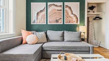 A modern living room with a grey sectional sofa, a wooden coffee table with a remote control, and three abstract art pieces on the wall.