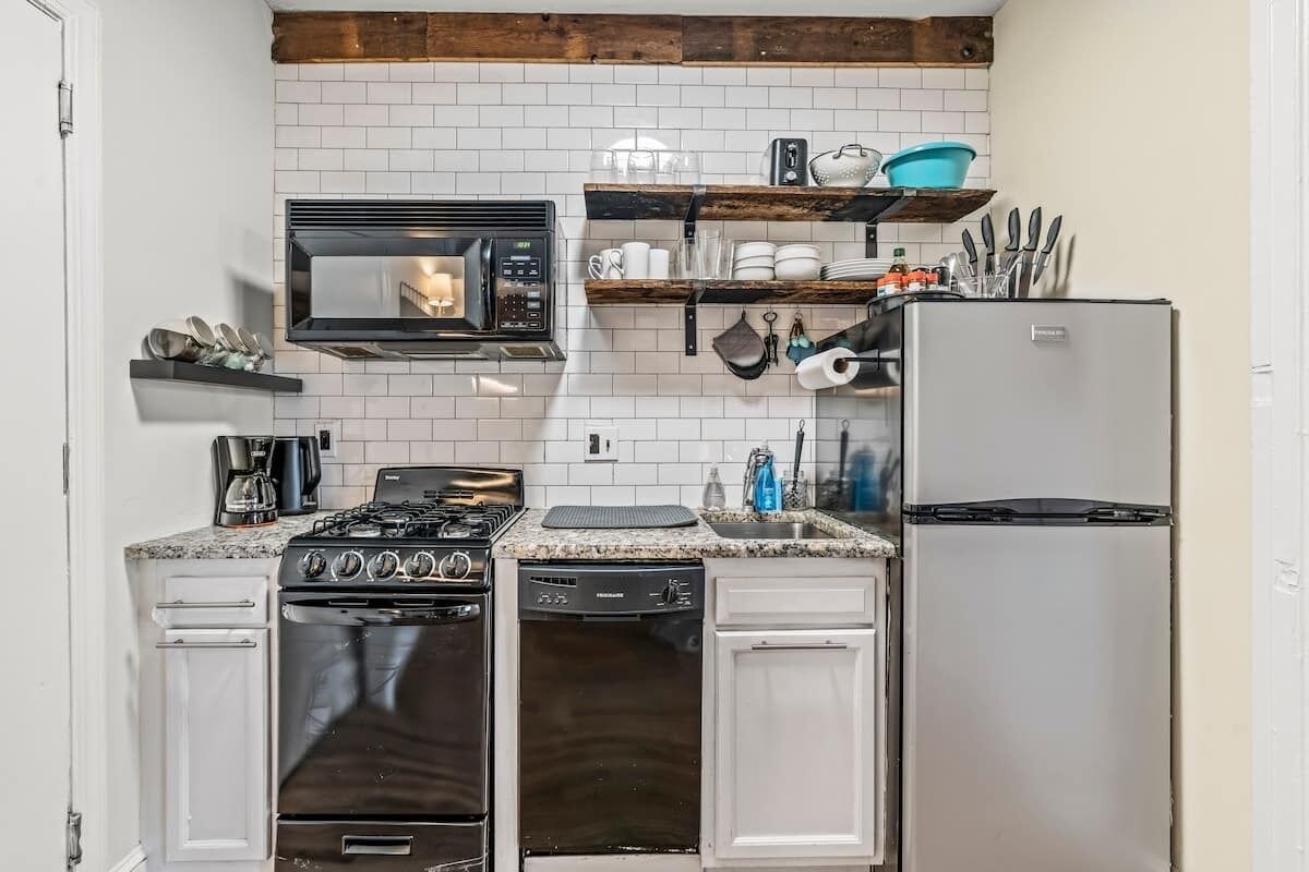 A compact kitchen with white cabinetry, a built-in microwave, a gas stove, a dishwasher, and a refrigerator.