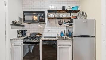 A compact kitchen with white cabinetry, a built-in microwave, a gas stove, a dishwasher, and a refrigerator.
