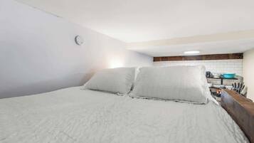 A bedroom with a bed, pillows, a small kitchenette with a sink and a blue bowl.