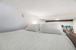 Ein Schlafzimmer mit einem Bett, Kissen und einer kleinen Küchenzeile mit einem Spülbecken und einer blauen Schüssel.