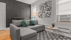 A modern living room with a grey sectional sofa, a black brick accent wall, a geometric patterned rug, and a small round side table with a plant. - Huge Desk - Central - Soak Tub - Walkscore 98 (Philadelphia)