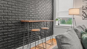 A room with a brick wall, a window with blinds, a bar stool, a lamp, and a couch. - Huge Desk - Central - Soak Tub - Walkscore 98 (Philadelphia)