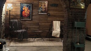 A cozy room with a brick archway, a round table, two chairs, a small table with a candle, and vintage posters on the wall. - Rising Hall B&B (Coatesville)