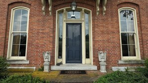 A brick building with a central entrance, two side windows, and a decorative light fixture above the door. - Rising Hall B&B (Coatesville)