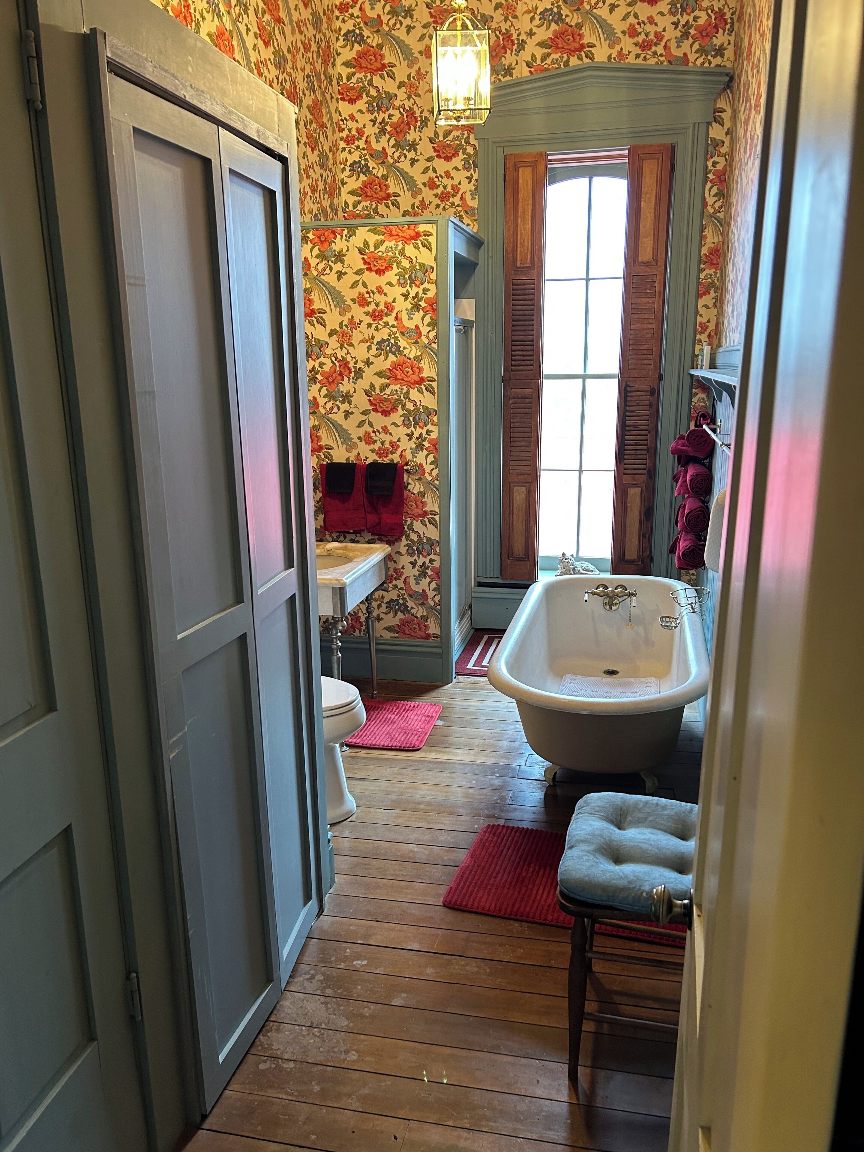 A narrow hallway leading to a bathroom with a vintage bathtub, wooden flooring, and floral wallpaper.