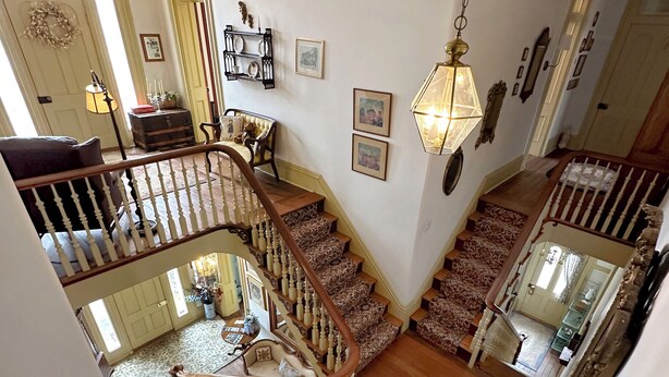 A multi-level interior with a staircase, a dining area, and a living room with a sofa and a table. - Rising Hall B&B (Coatesville)