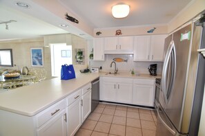 A kitchen with white cabinets, a stainless steel refrigerator, and a tiled floor. - 20% off week of July 25-Aug. 1.  3BR OF condo. Ocean Drive. Pool. (North Myrtle Beach)