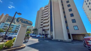 A hotel with a prominent sign, multiple floors, and a parking lot with cars. - 20% off week of July 25-Aug. 1.  3BR OF condo. Ocean Drive. Pool. (North Myrtle Beach)