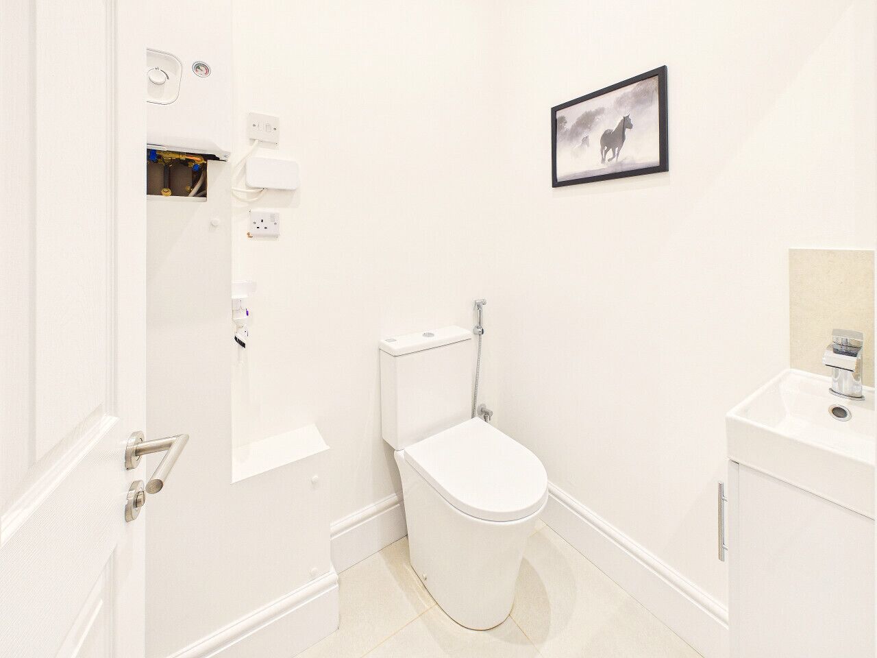 A white bathroom with a toilet, a sink, and a framed picture on the wall.