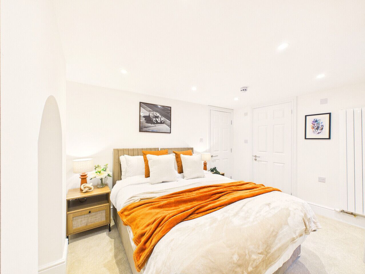 Ein Schlafzimmer mit Bett, Nachttisch, Lampe und gerahmten Bildern an der Wand.