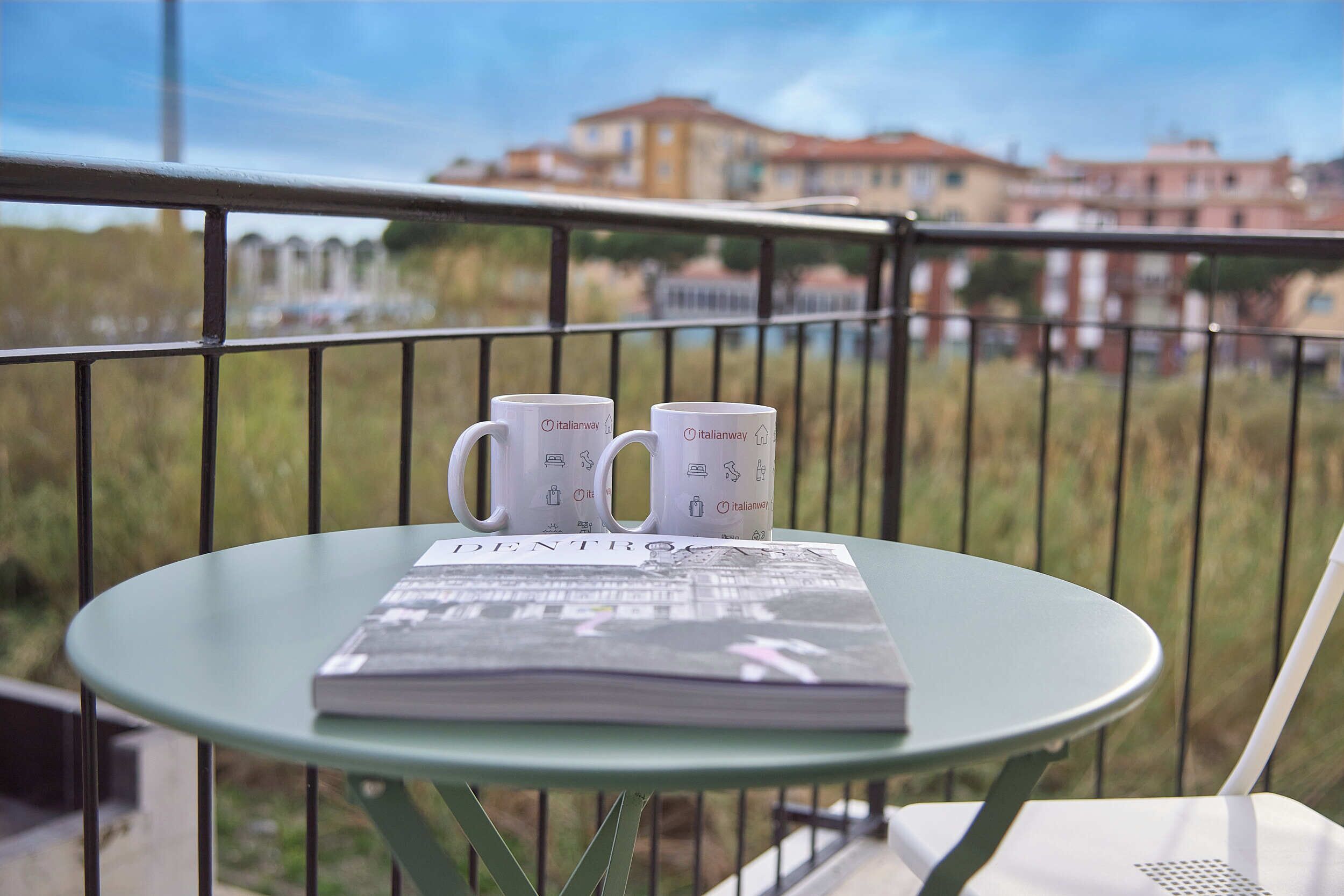 A balcony with a table holding two Italianway mugs and a magazine.