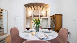 Un comedor con una mesa redonda, dos sillas, un florero con flores y dos copas de vino tinto.