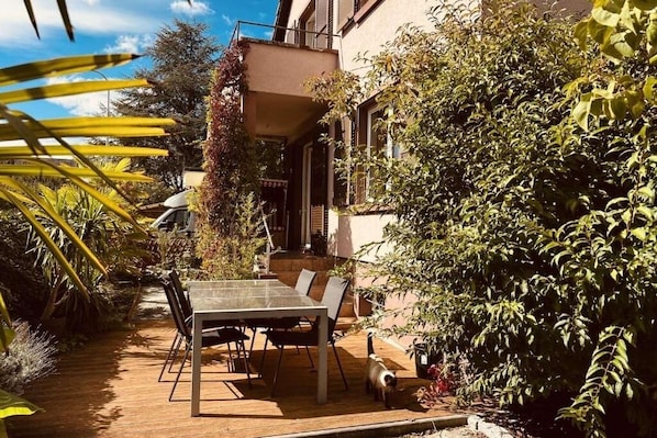 Un patio con mesa y sillas, rodeado de vegetación y un edificio.