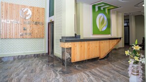 Zona de recepción de un hotel con un mostrador de madera, un letrero en la pared y un panel decorativo verde.