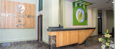 A hotel reception area with a wooden reception desk, a wall-mounted sign, and a green decorative panel.
